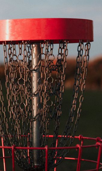 A resident from Elm Hollow Apartments enjoys an evening round of disc golf, skillfully aiming a frisbee at the red basket cast in the warm glow of sunset.