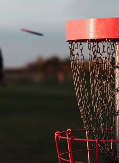 A resident from Elm Hollow Apartments enjoys an evening round of disc golf, skillfully aiming a frisbee at the red basket cast in the warm glow of sunset.