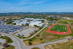 Aerial view of a large school campus with parking lots, sports fields, and the surrounding landscape, located just beyond the Elm Hollow Apartments.