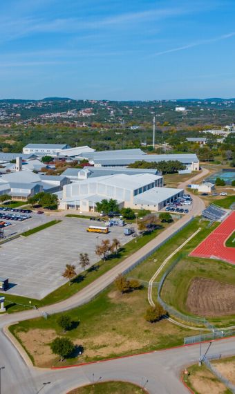 Aerial view of a large school campus with parking lots, sports fields, and the surrounding landscape, located just beyond the Elm Hollow Apartments.