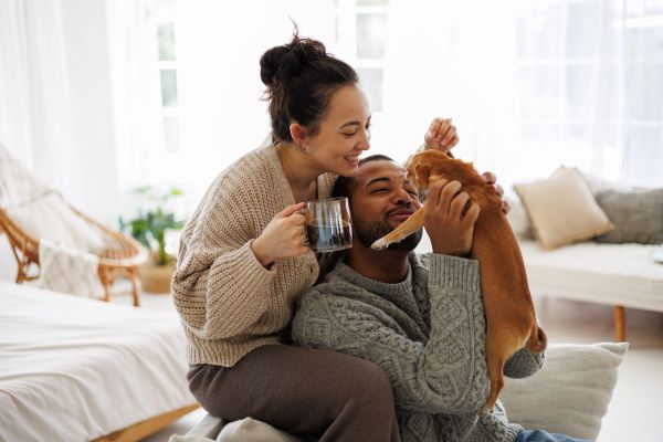 In their cozy Elm Hollow Apartments living room, a couple enjoys quality time with their dog. The woman savors a warm mug in hand, while the man playfully engages with their furry friend.