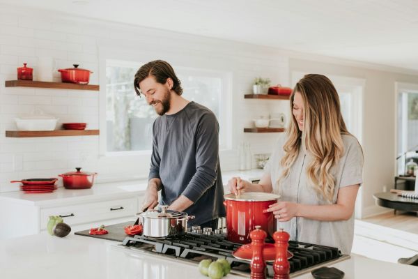 A man and woman cook in the bright kitchen of their Elm Hollow Apartments unit, using red cookware on the stove.